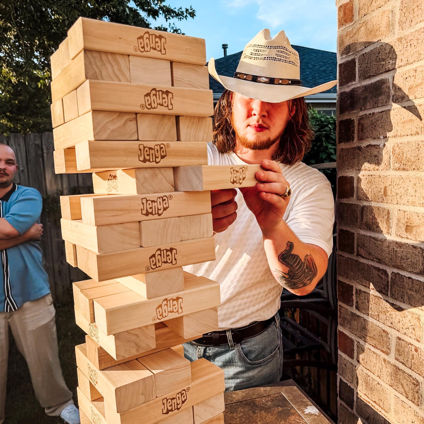 Man in cowboy hat at engagement party playing a giant jenga yard game rented near Fayetteville, AR